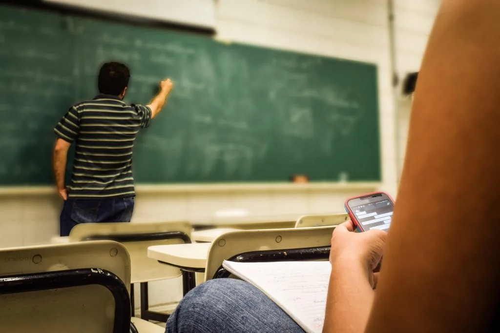 A teacher at a chalkboard, with a student seated in the foreground.