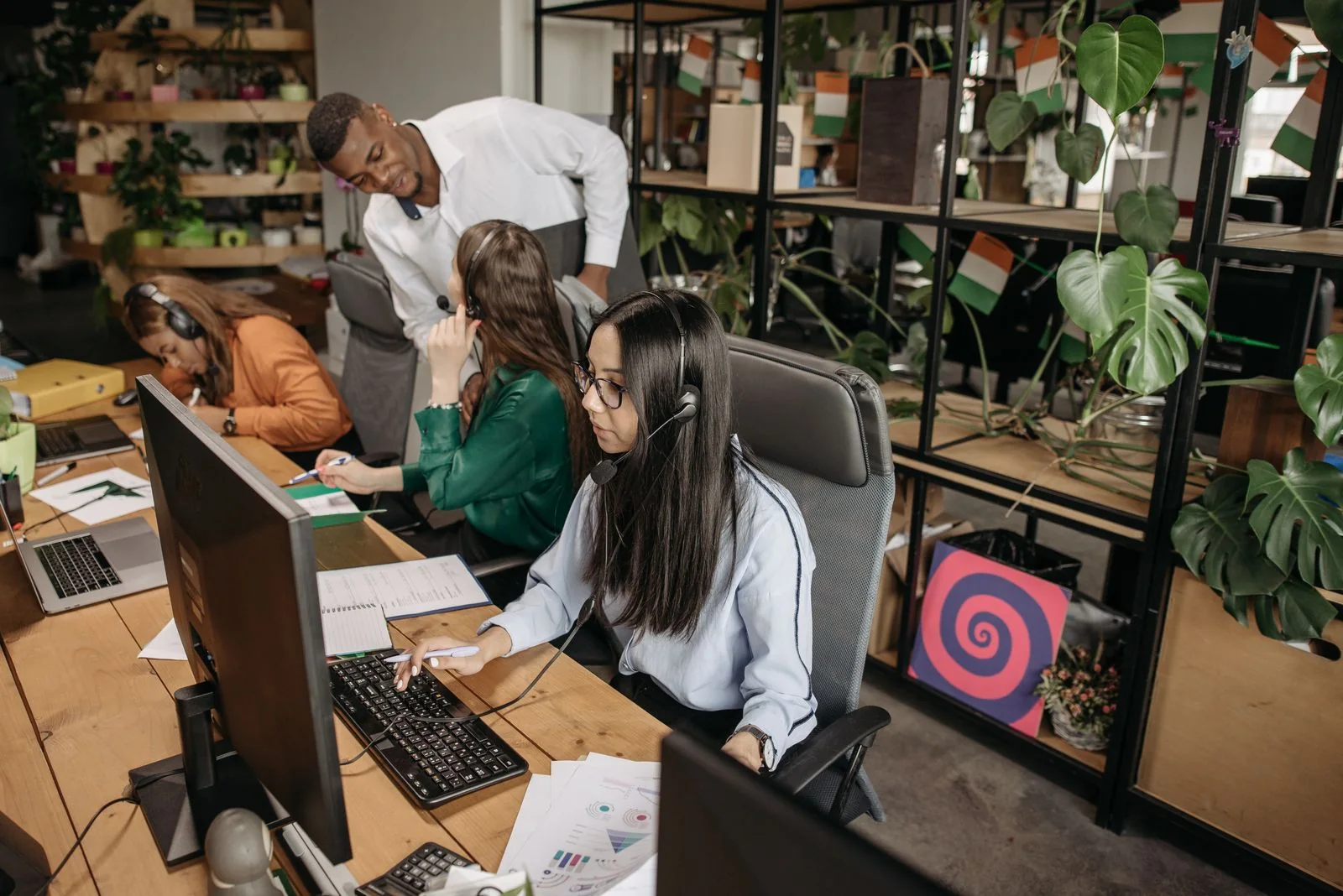 Colleagues using computers and headsets in a shared workspace.
